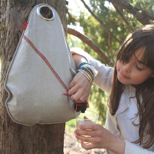 Jeune fille se servant à boire à partir d'une fontaine à boisson Obag' accrochée à un arbre