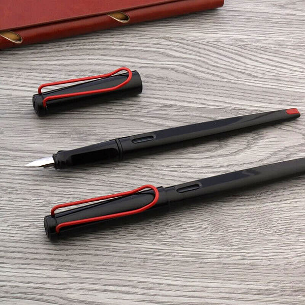 Un stylo plume long noir et rouge sur un support en bois à côté d'un carnet brun