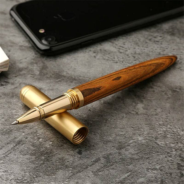Stylo à bille en bois et doré avec le capuchon détaché posé sur une table grise avec un téléphone portable